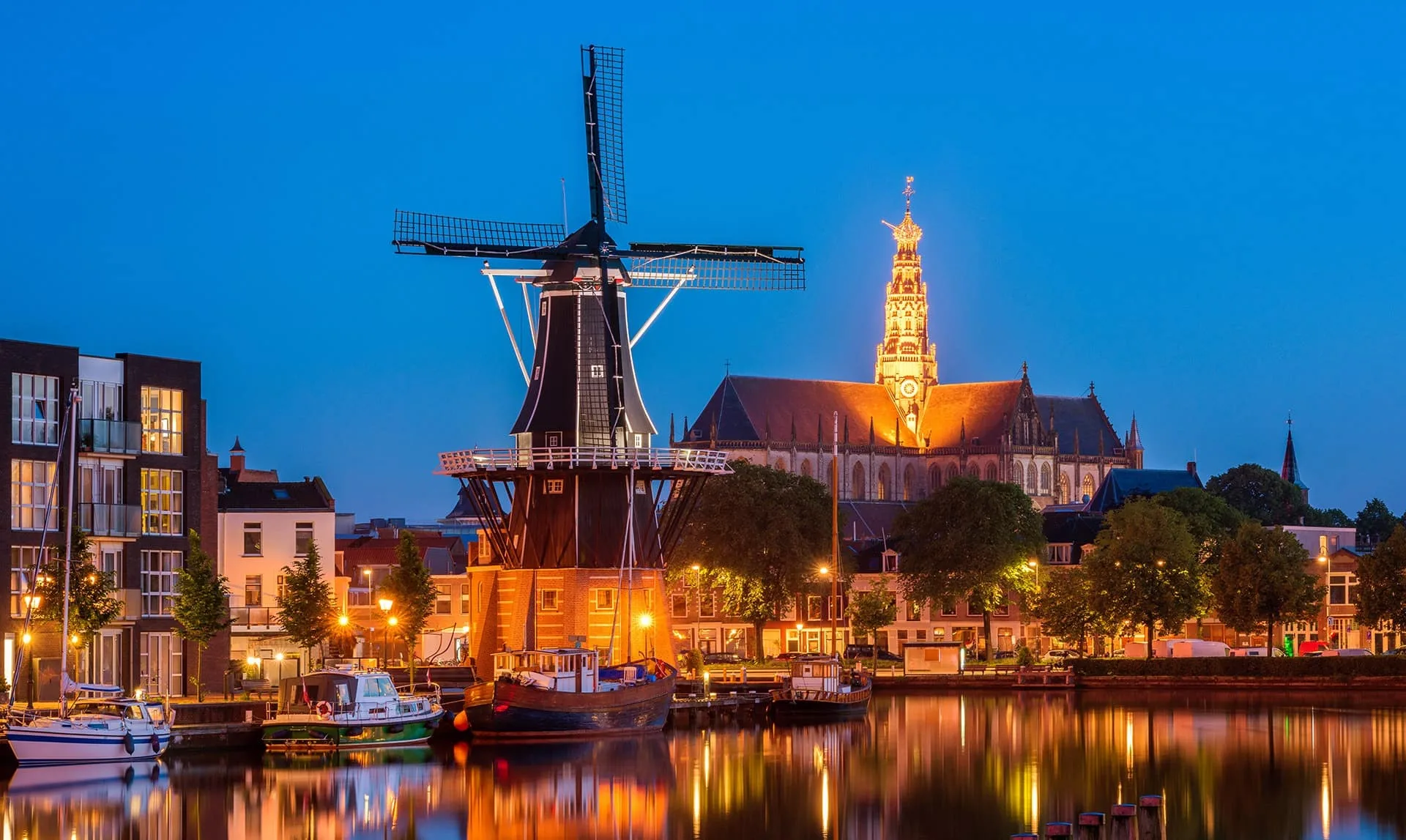 Haarlem windmill and church lit at night beside the Spaarne river